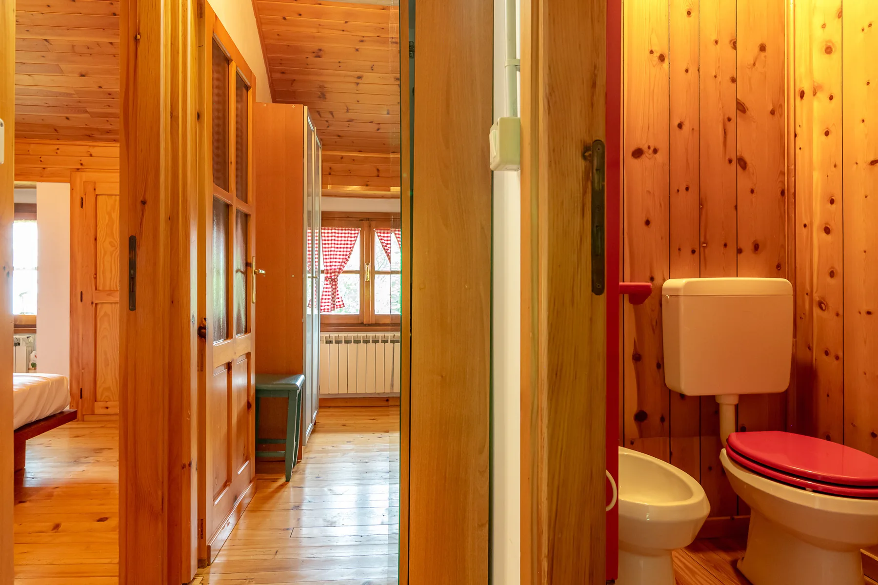 Un baño revestido de madera con inodoro y bidé junto a un pasillo.