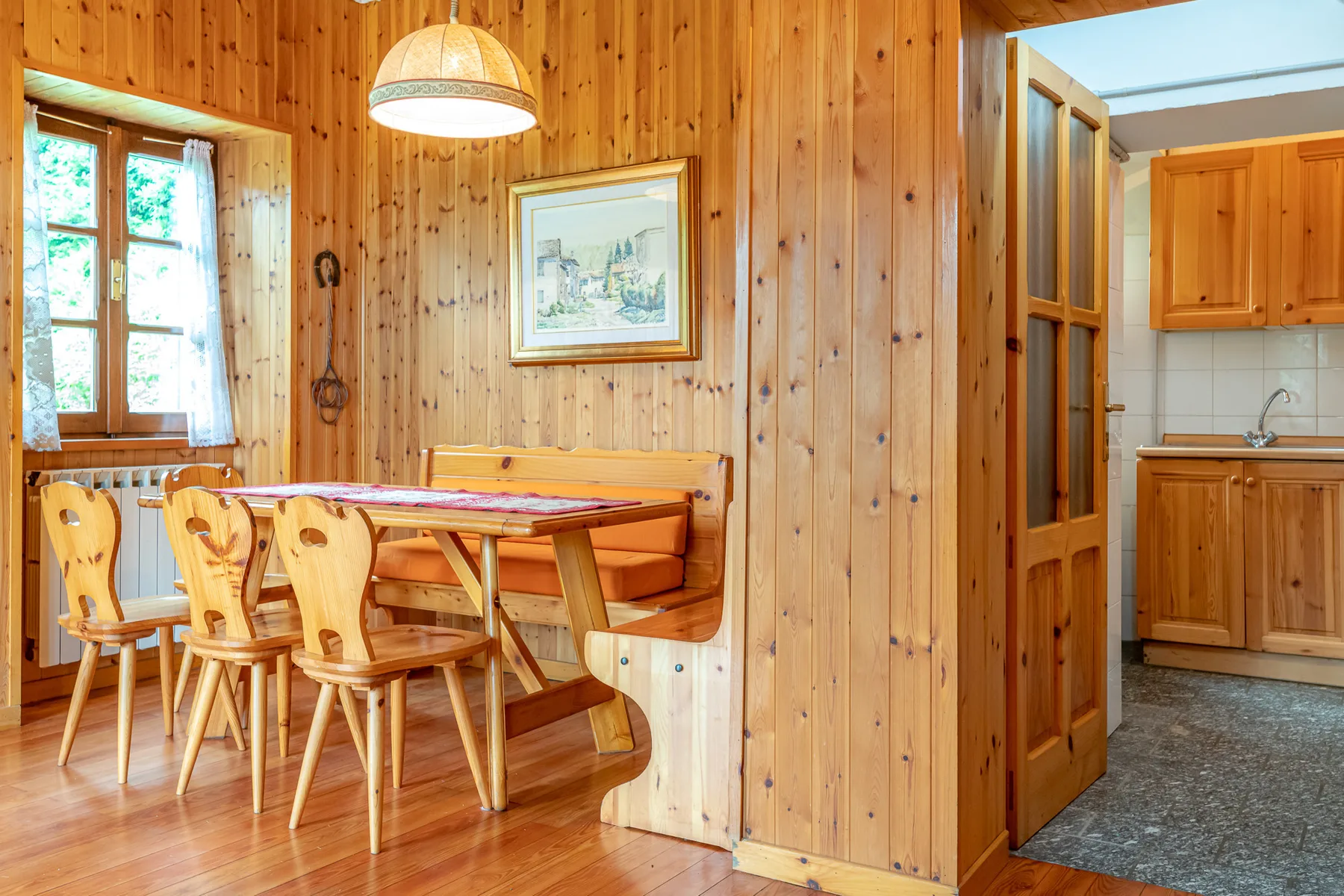 Un comedor revestido de madera con una mesa y asientos junto a una cocina abierta.