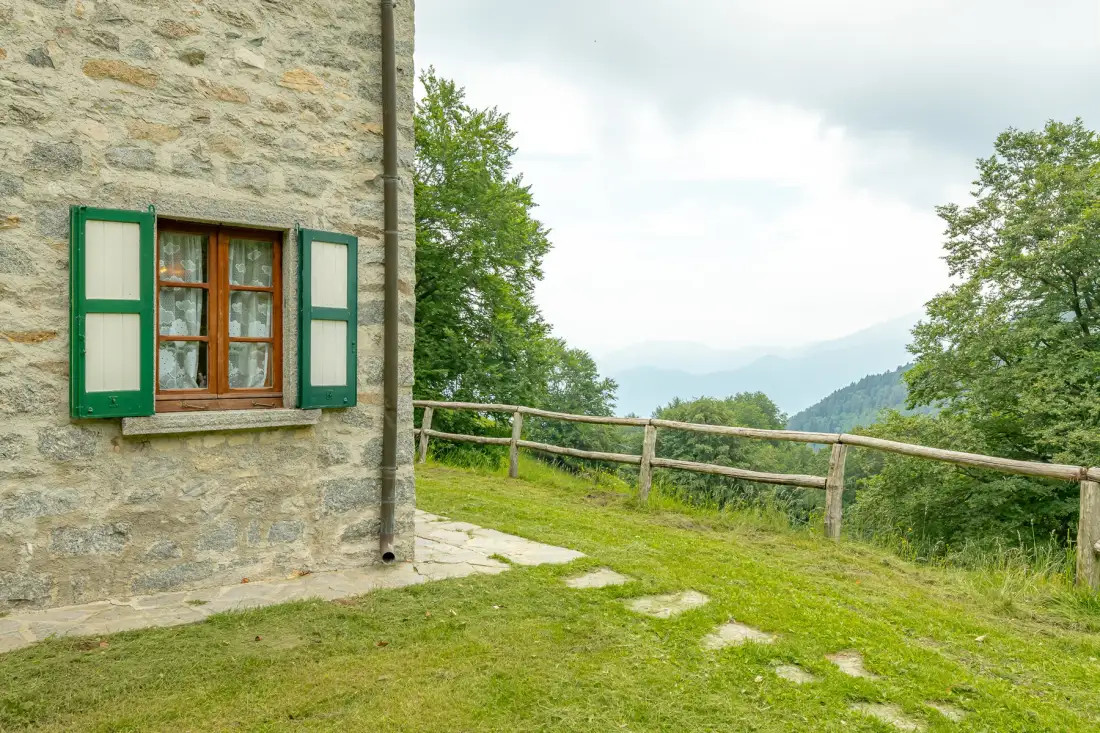 Un edificio de piedra junto a un patio de césped y una cerca de madera con vistas a colinas.