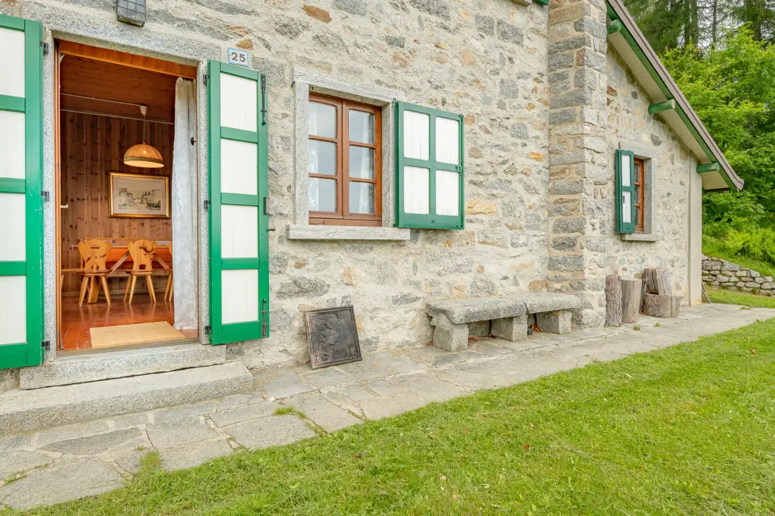 Exterior de un edificio de piedra con contraventanas verdes y una puerta abierta.