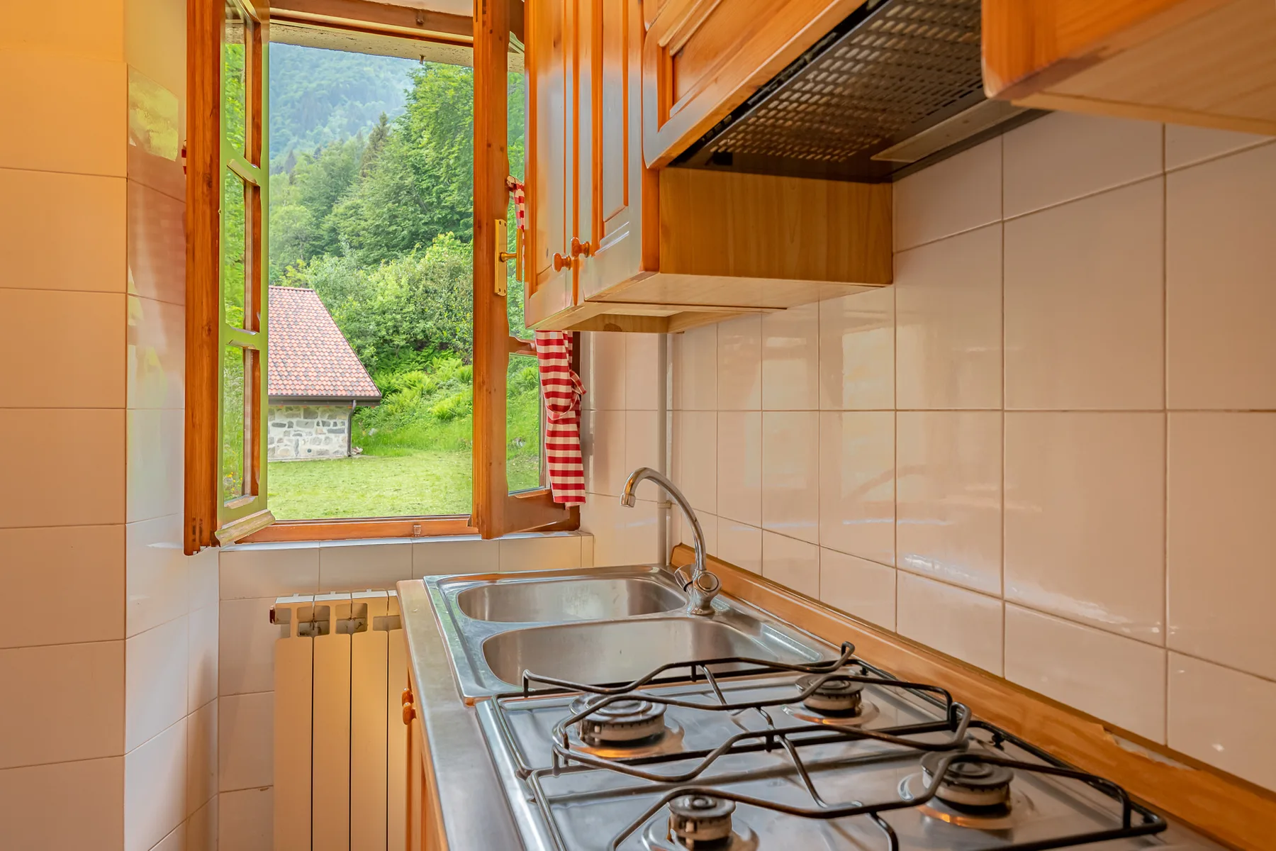 Una cocina compacta con estufa de gas, fregadero y una ventana abierta con vista al verdor.