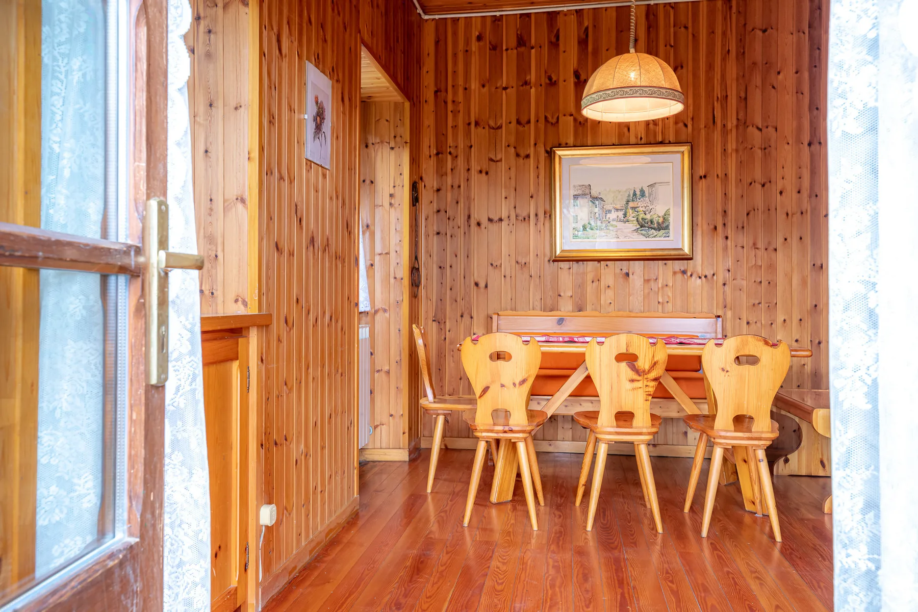 Comedor revestido de madera con una mesa, sillas y una lámpara colgante.