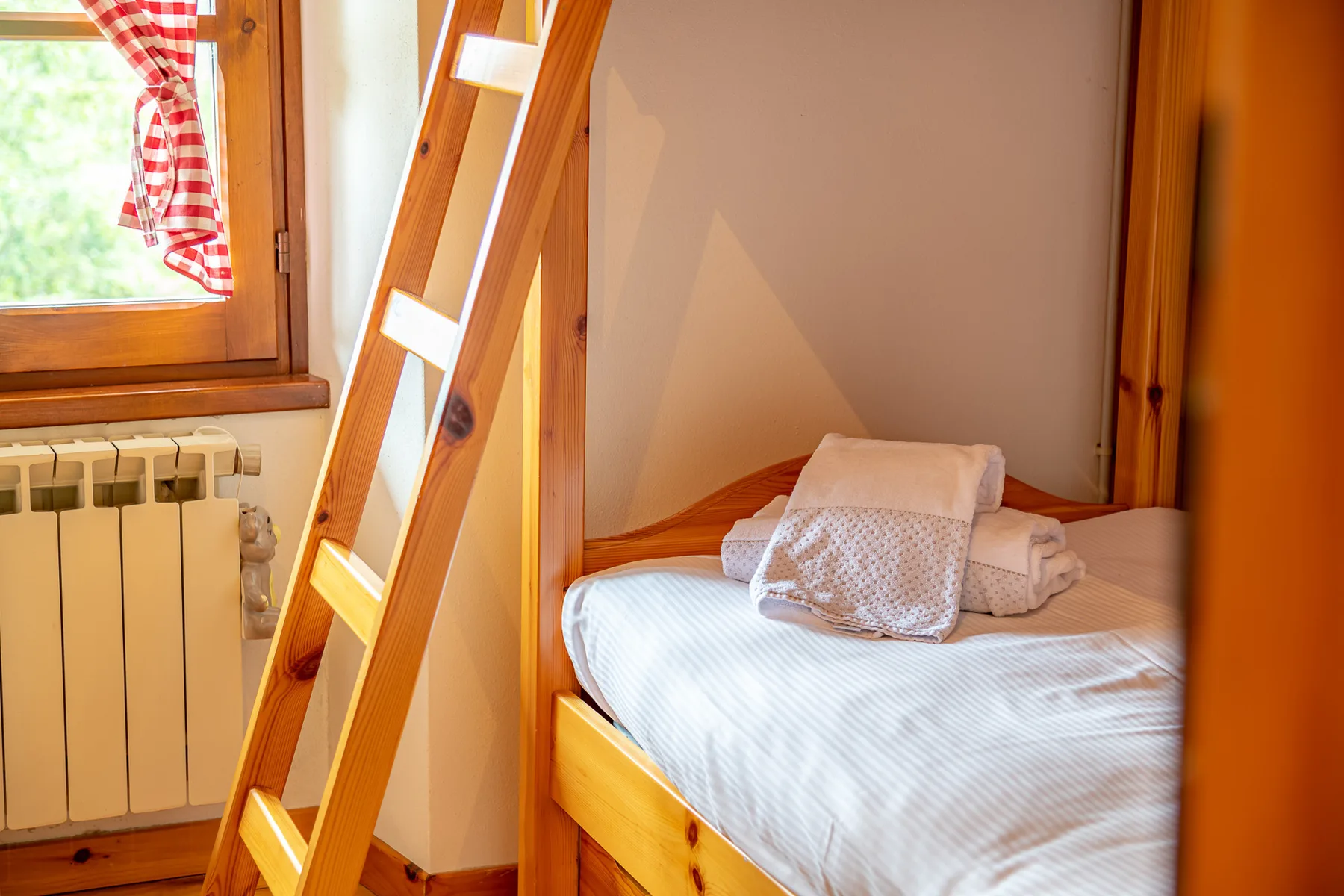 Un dormitorio pequeño con una litera de madera y ropa de cama doblada.