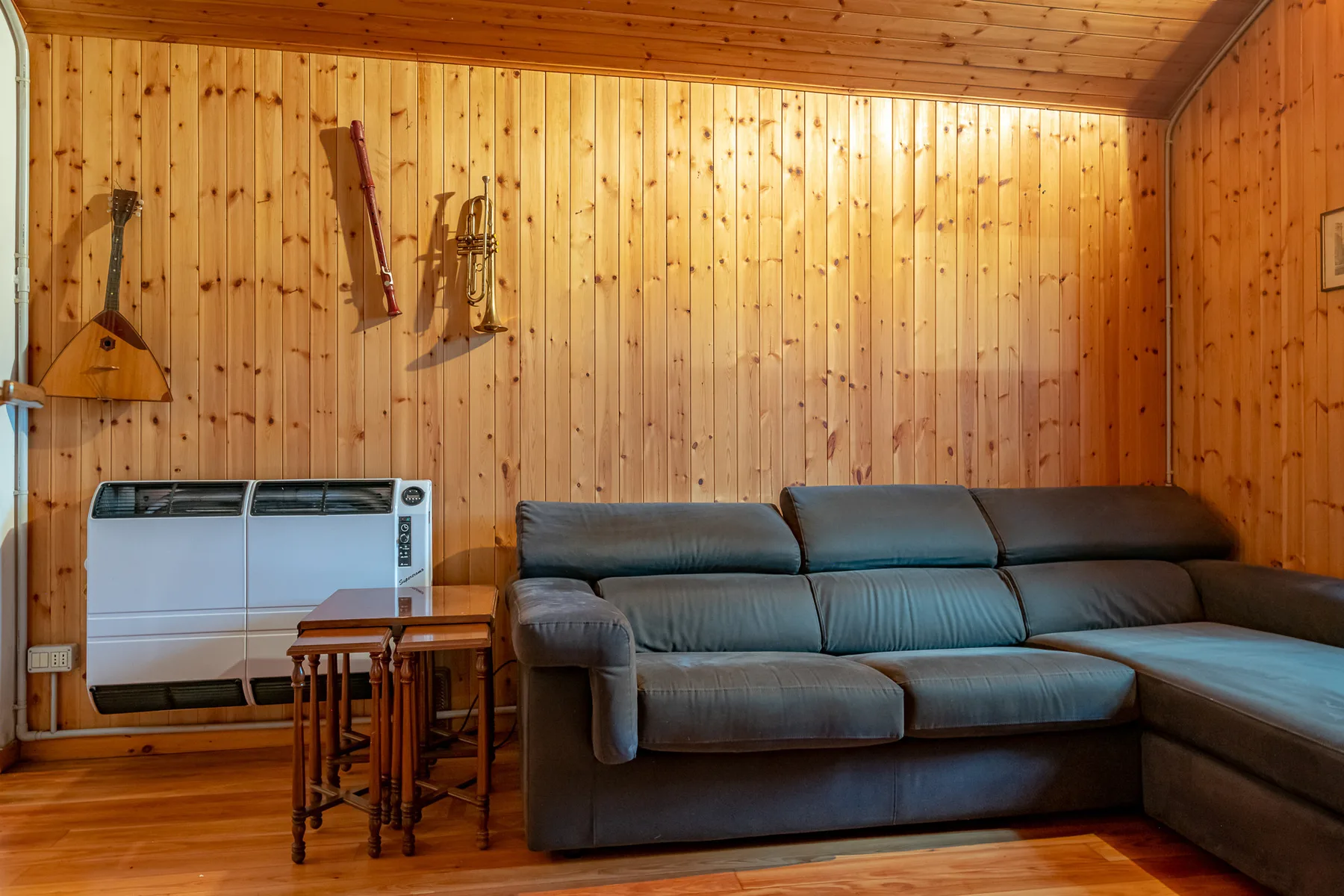 Sala de estar revestida de madera con sofá seccional y calefactor de pared.