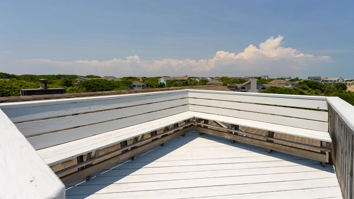 Una terraza blanca en la azotea con asientos integrados da a zonas verdes y casas lejanas.