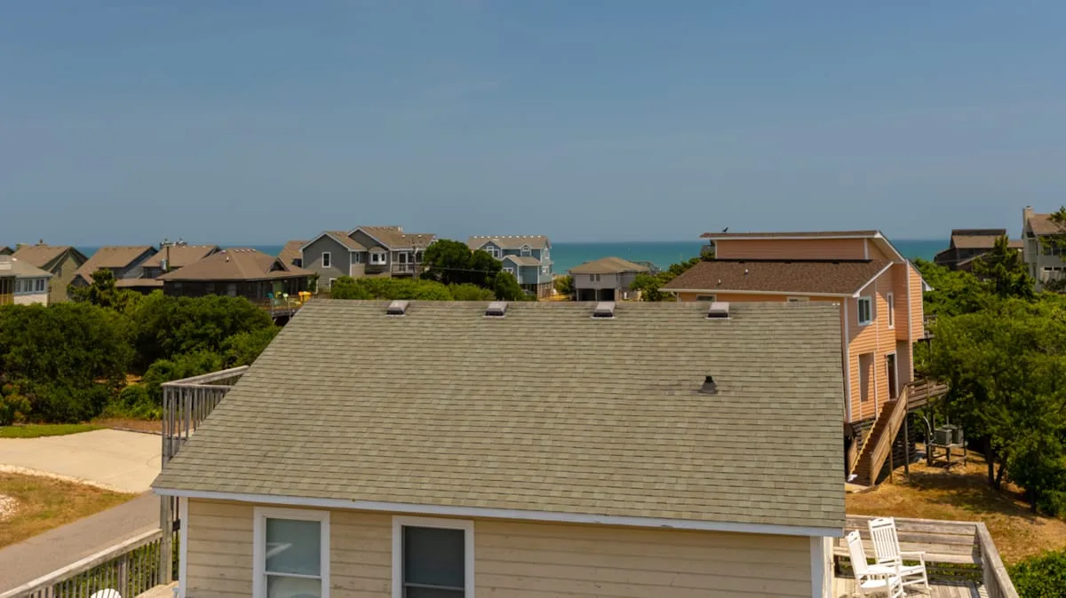 A coastal residential neighborhood with a large shingled roof in the foreground.