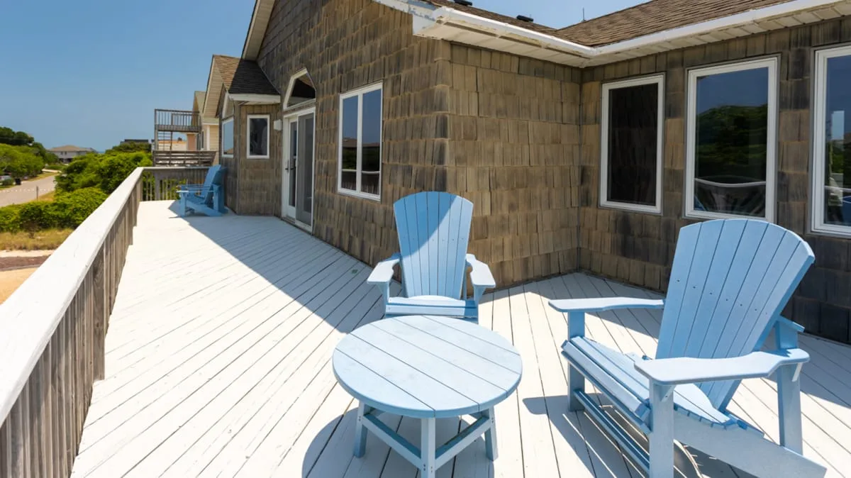 Una terraza de madera soleada junto a un edificio tiene asientos azules y una mesa pequeña.