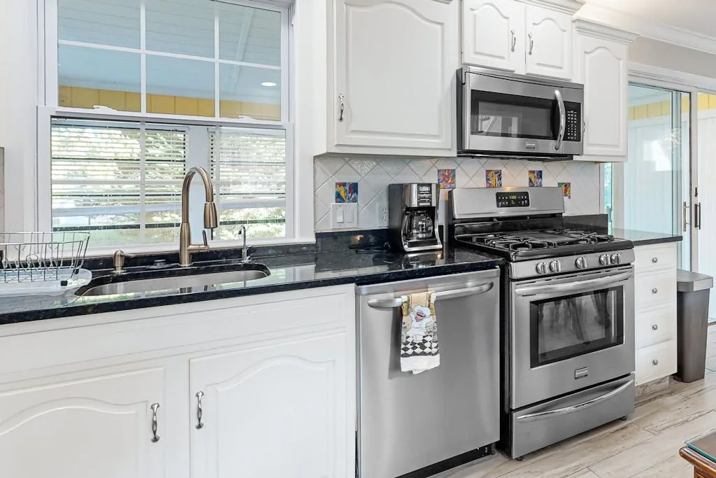 A bright kitchen with white cabinetry, dark countertops, and stainless steel appliances.