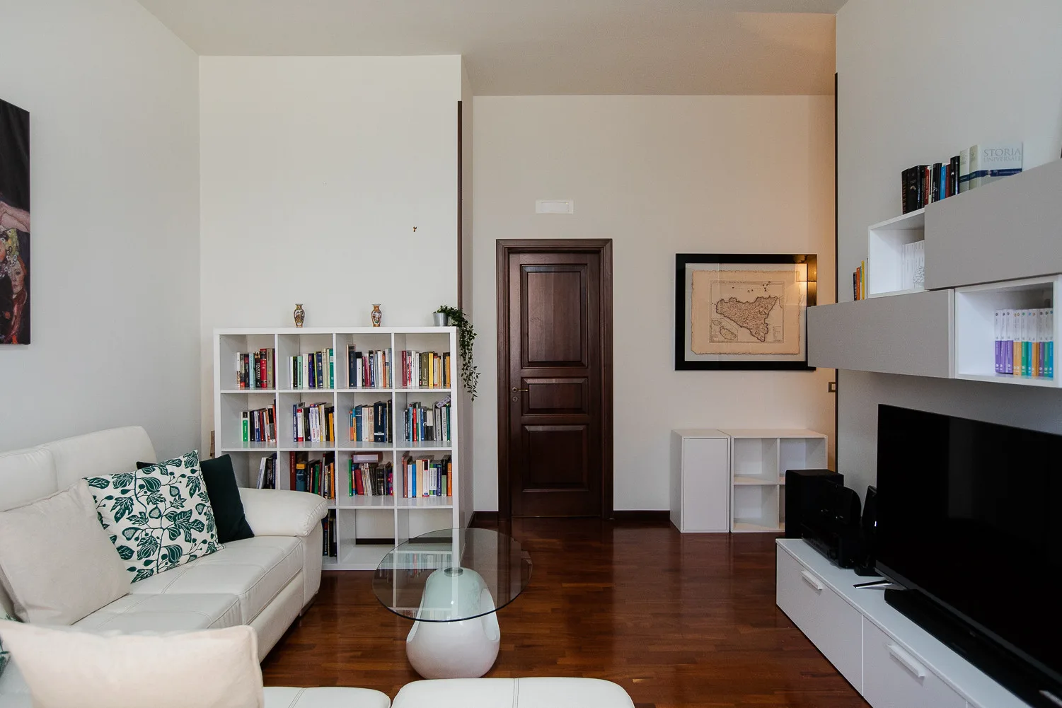 A living room with white seating, bookshelves, and a television.