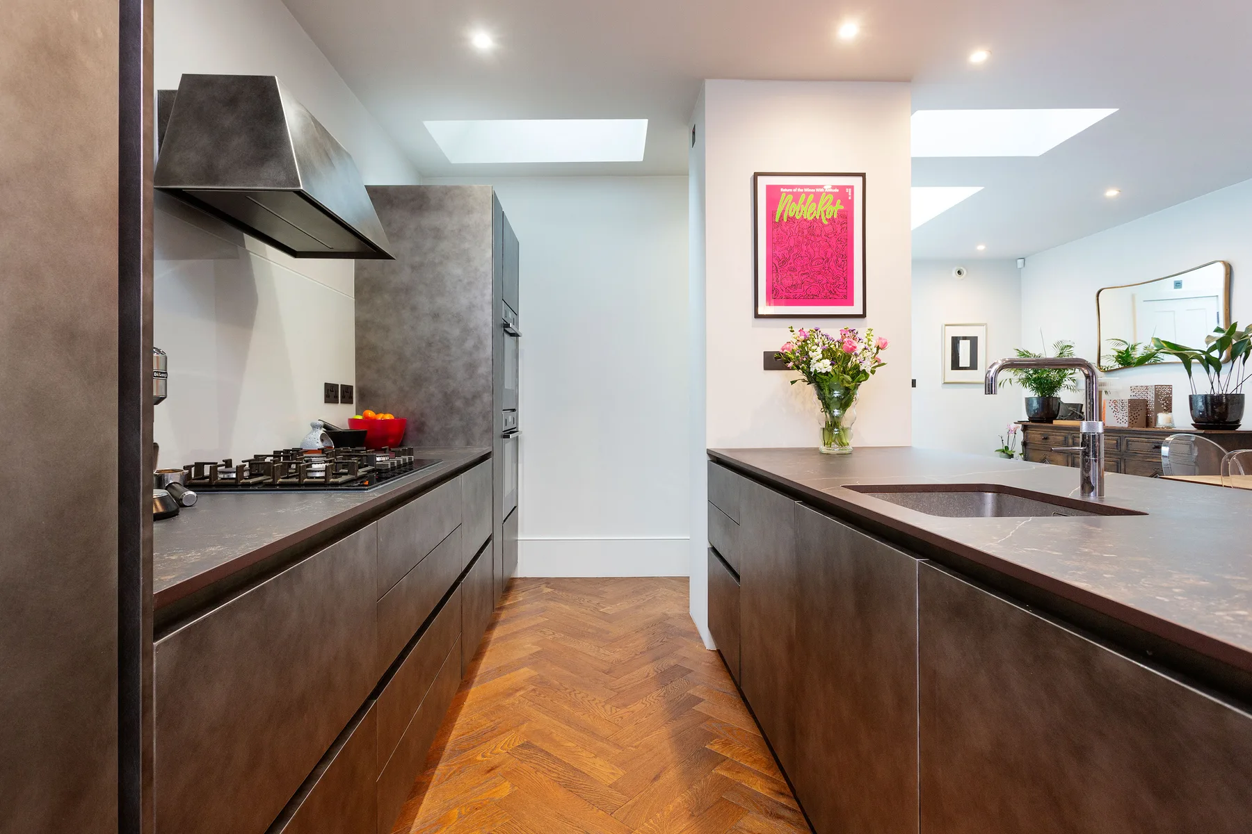 A modern kitchen with dark cabinetry, a central island, and a vase of flowers.