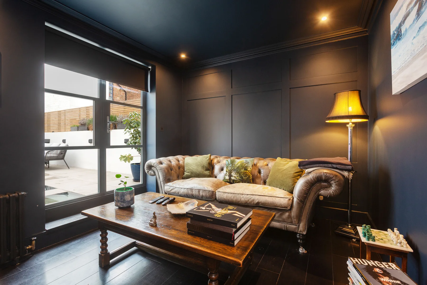Una sala de estar oscura con sofá de cuero, mesa de centro y una ventana grande.