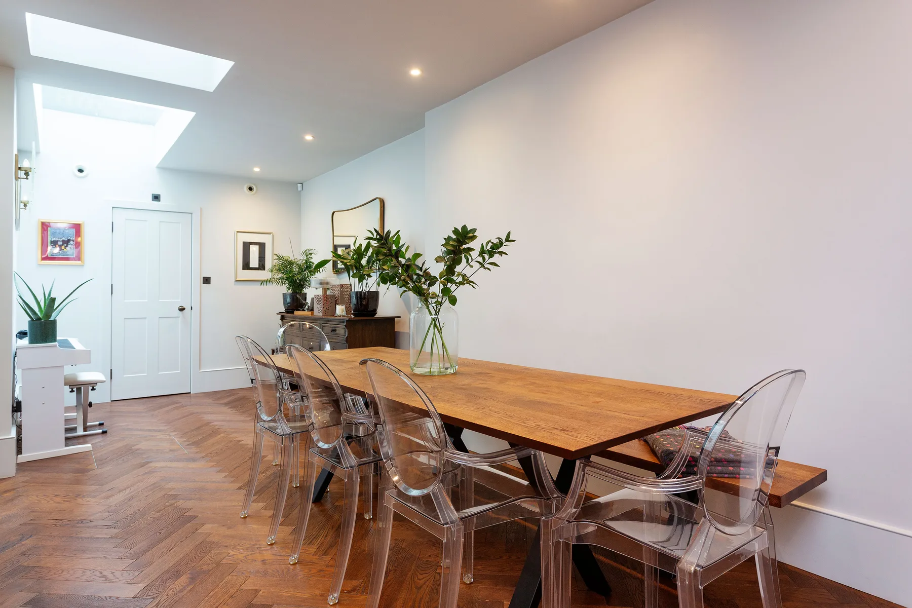 Un comedor luminoso con una mesa larga de madera y asientos transparentes.