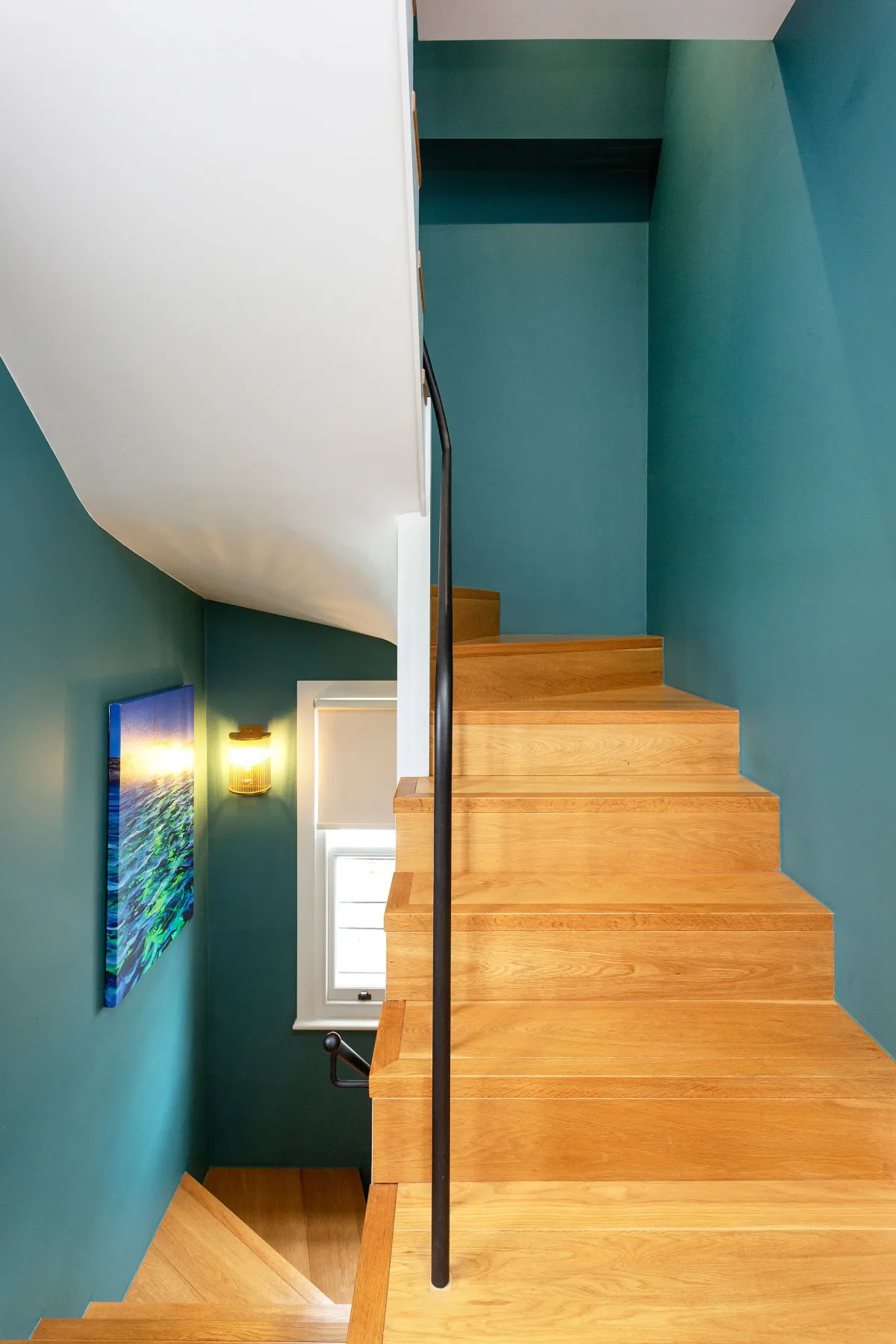 A wooden staircase rises between teal walls, with a slim dark handrail.