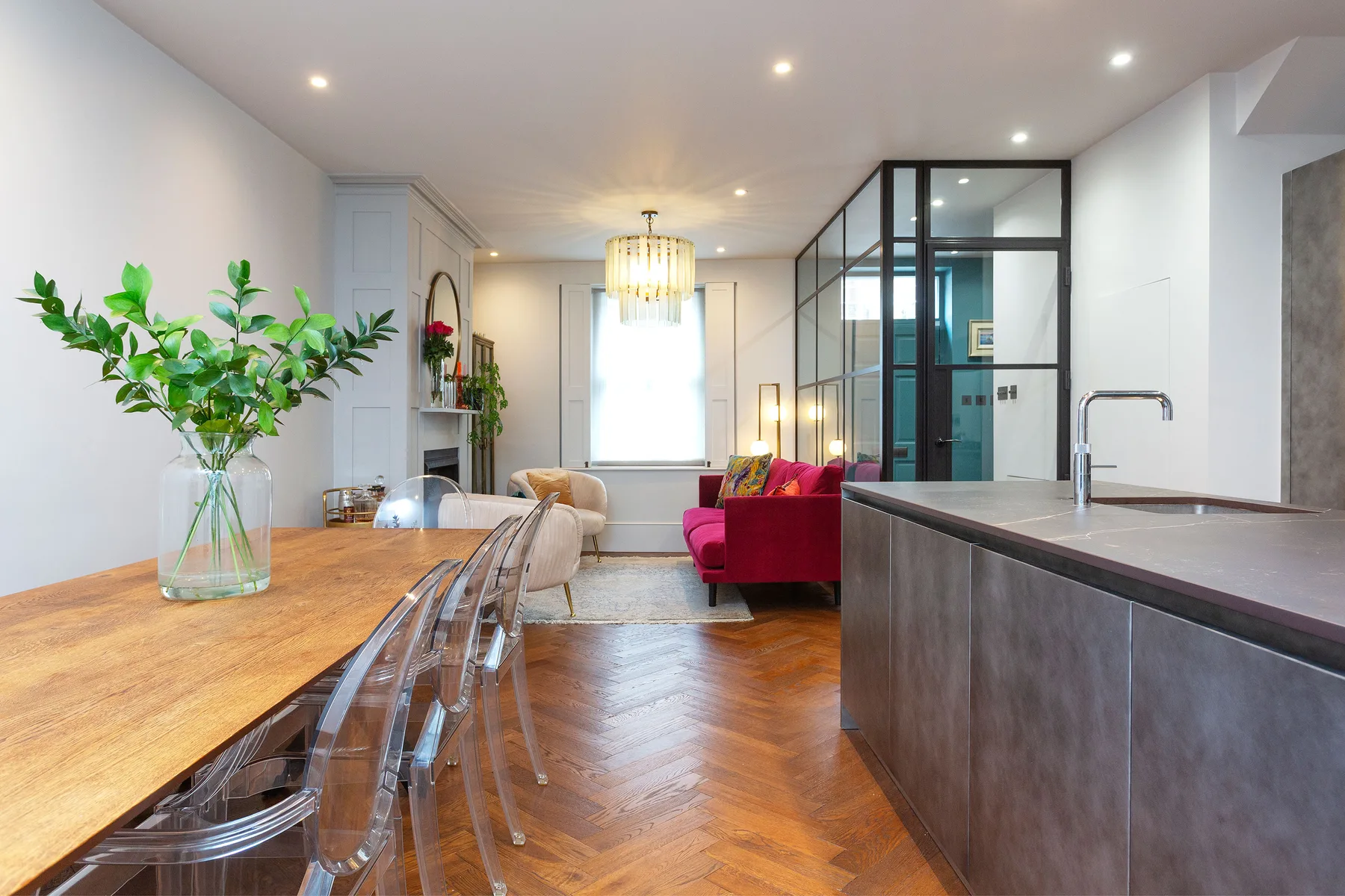 An open-plan dining and living area with a long wooden table and red seating.