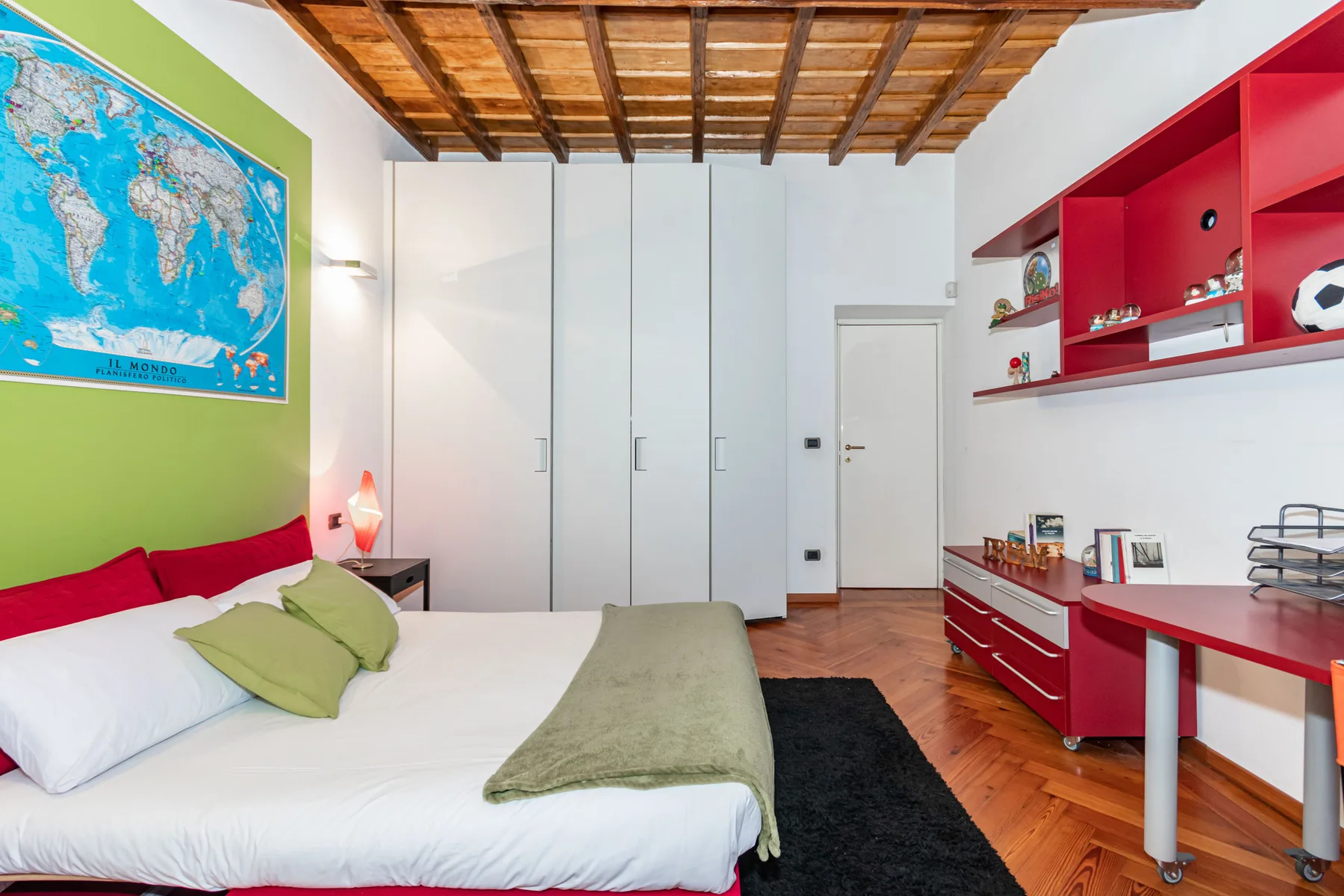 A bedroom with a bed, tall white wardrobes, and red built-in shelving.