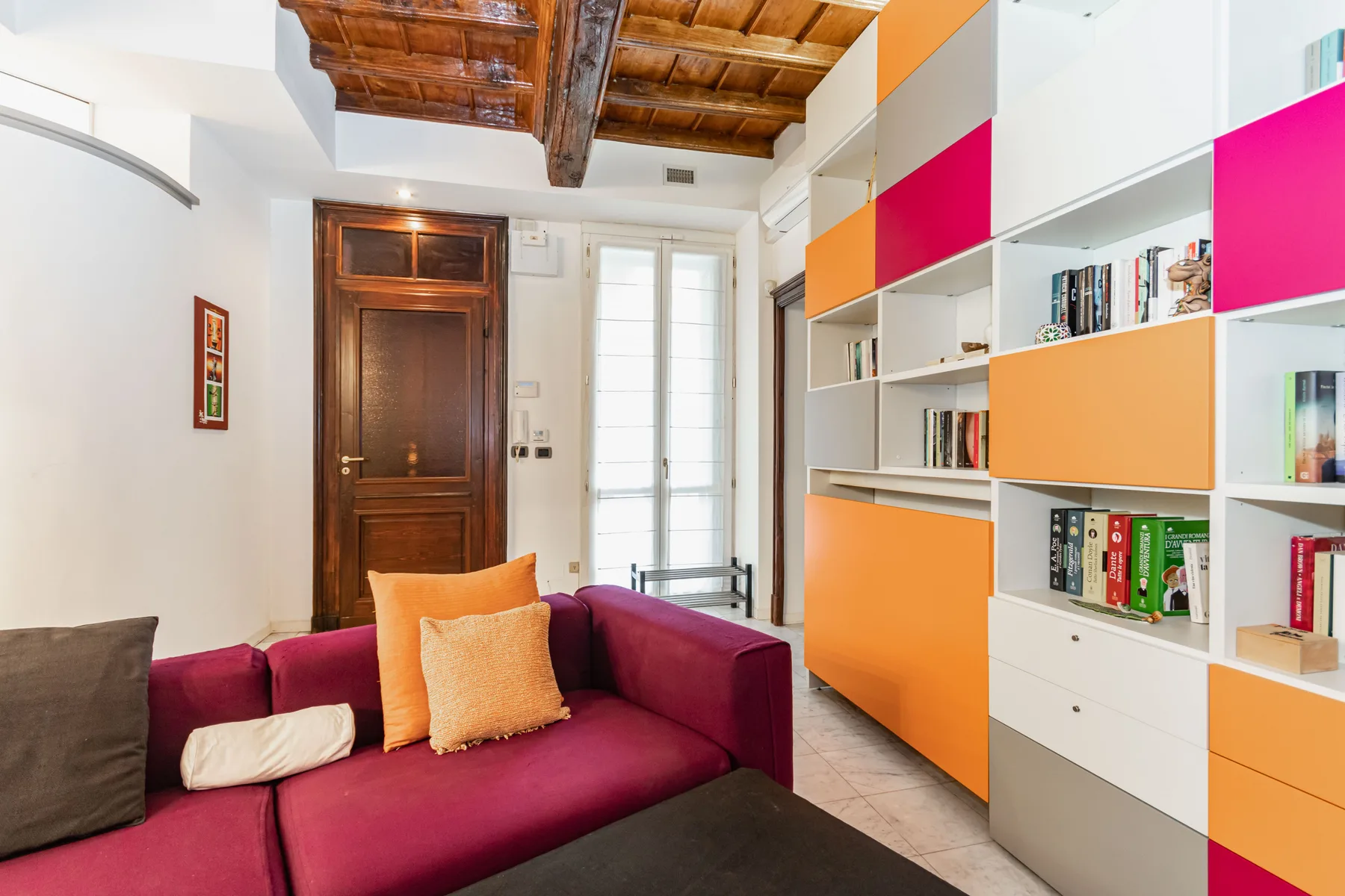 A colorful living room with magenta seating and built-in shelves.