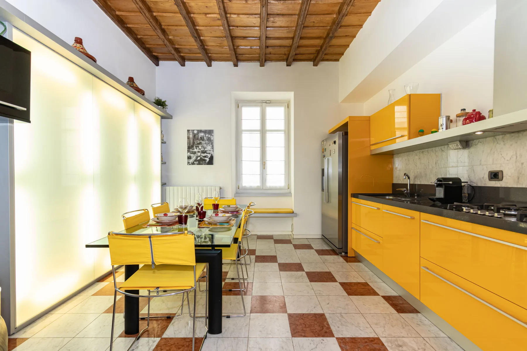 A bright kitchen with yellow cabinetry, a dining table, and a wood-beamed ceiling.
