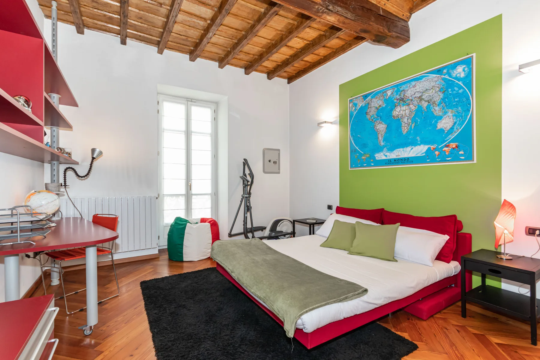 A bedroom with a red bed, green accent wall, and colorful world map.