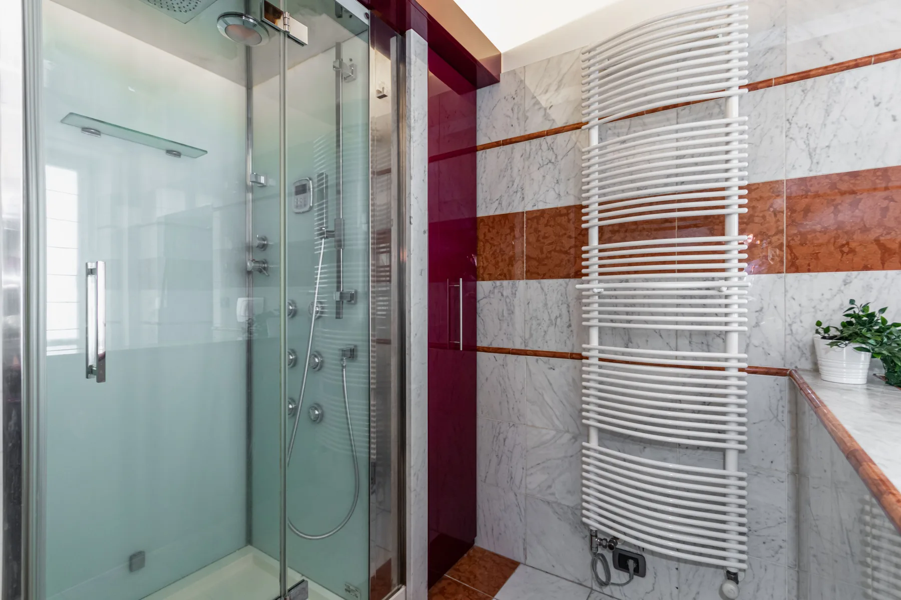 A tiled bathroom with a glass shower and a white heated towel rail.