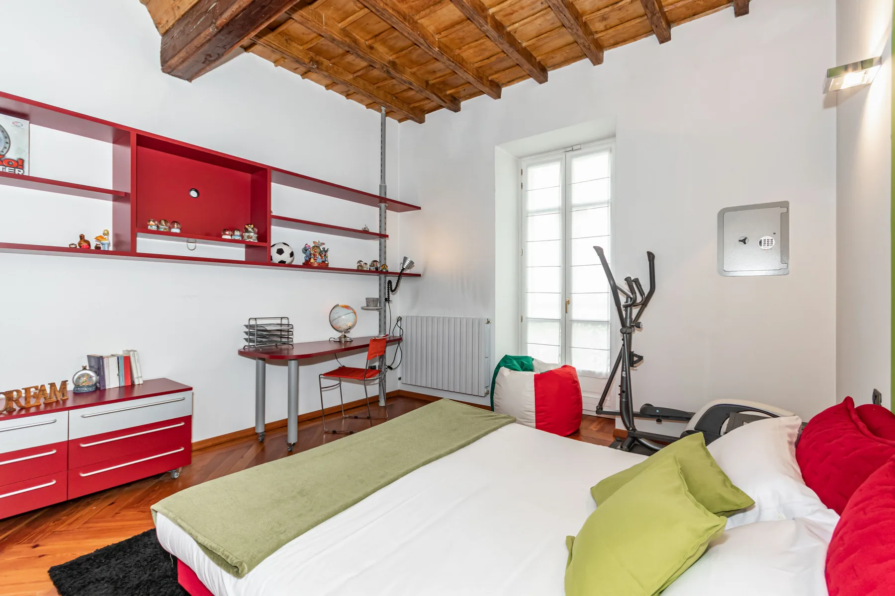A bedroom with a bed, red cabinetry, and exercise equipment.