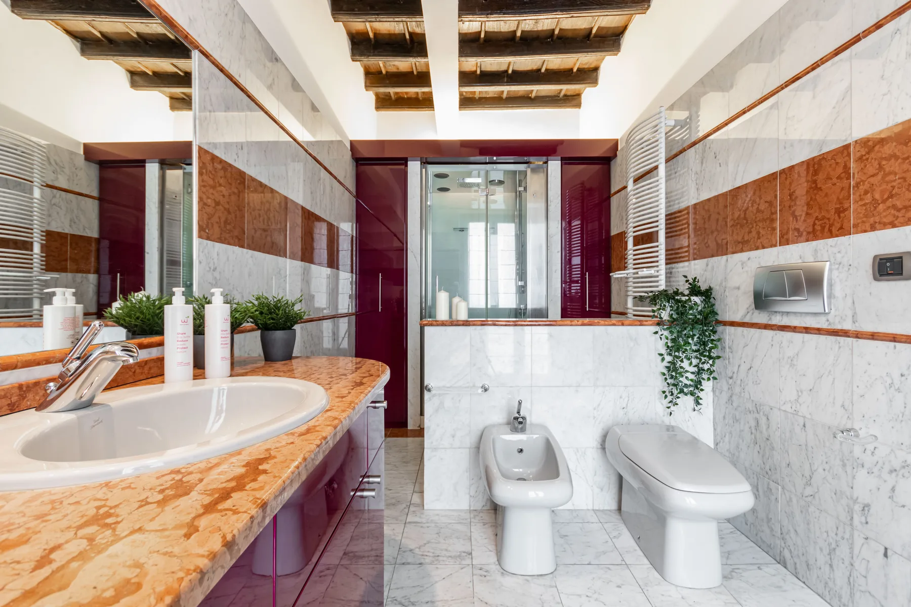 A bright bathroom with a marble vanity, sink, toilet, and bidet.