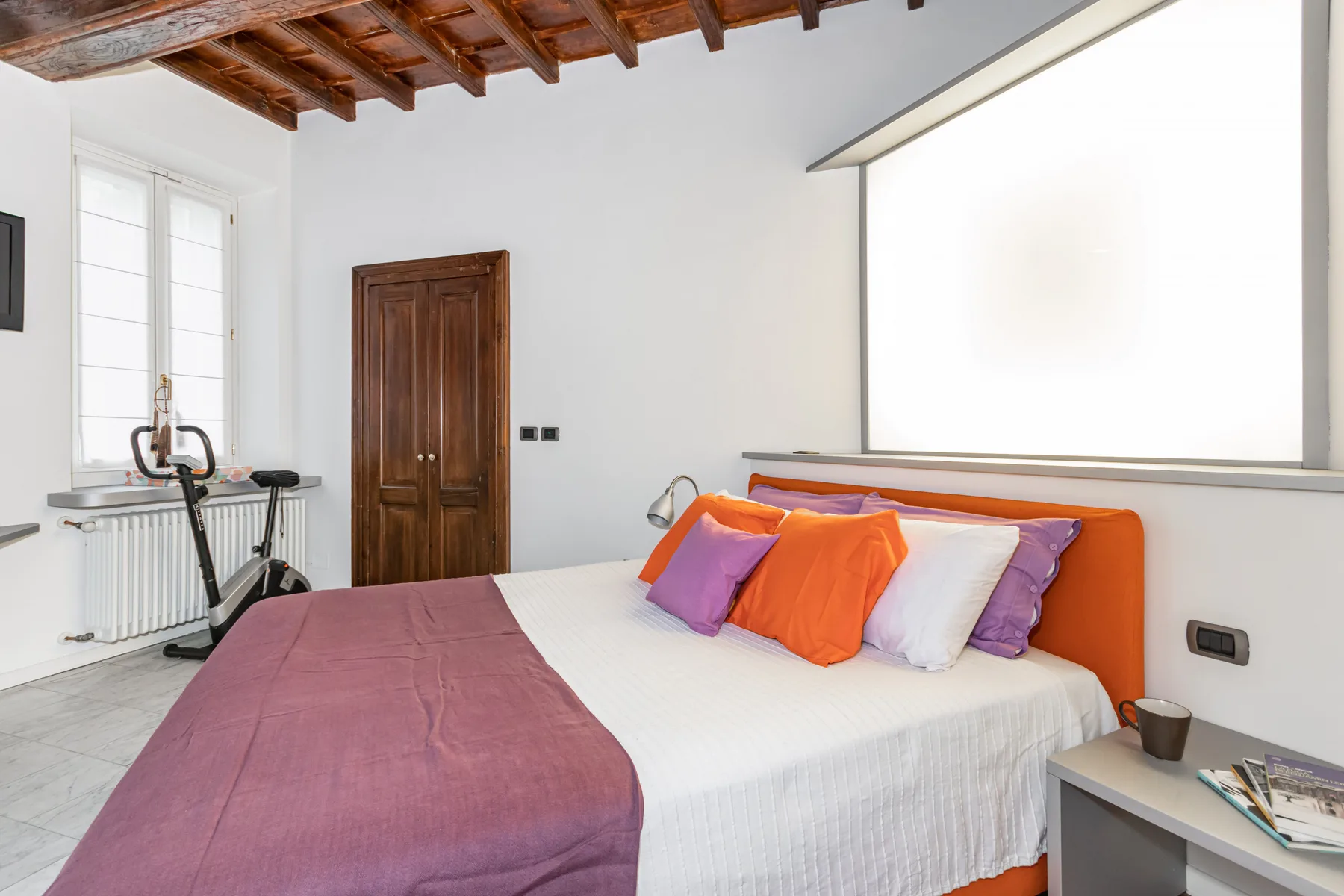 Bedroom with a bed, colorful pillows, and a large bright window.