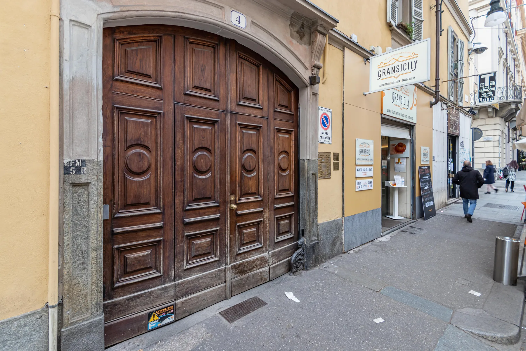 A city sidewalk runs past a large wooden entrance beside a storefront.