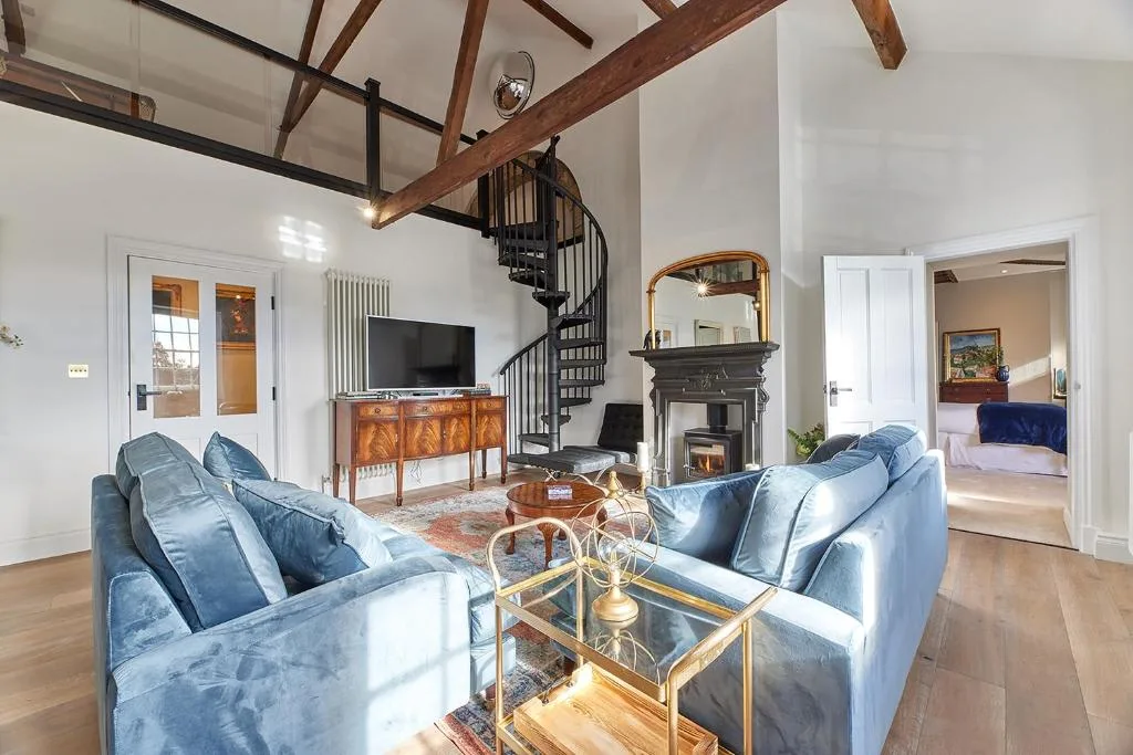 A living room with blue seating, a fireplace, and a spiral staircase.