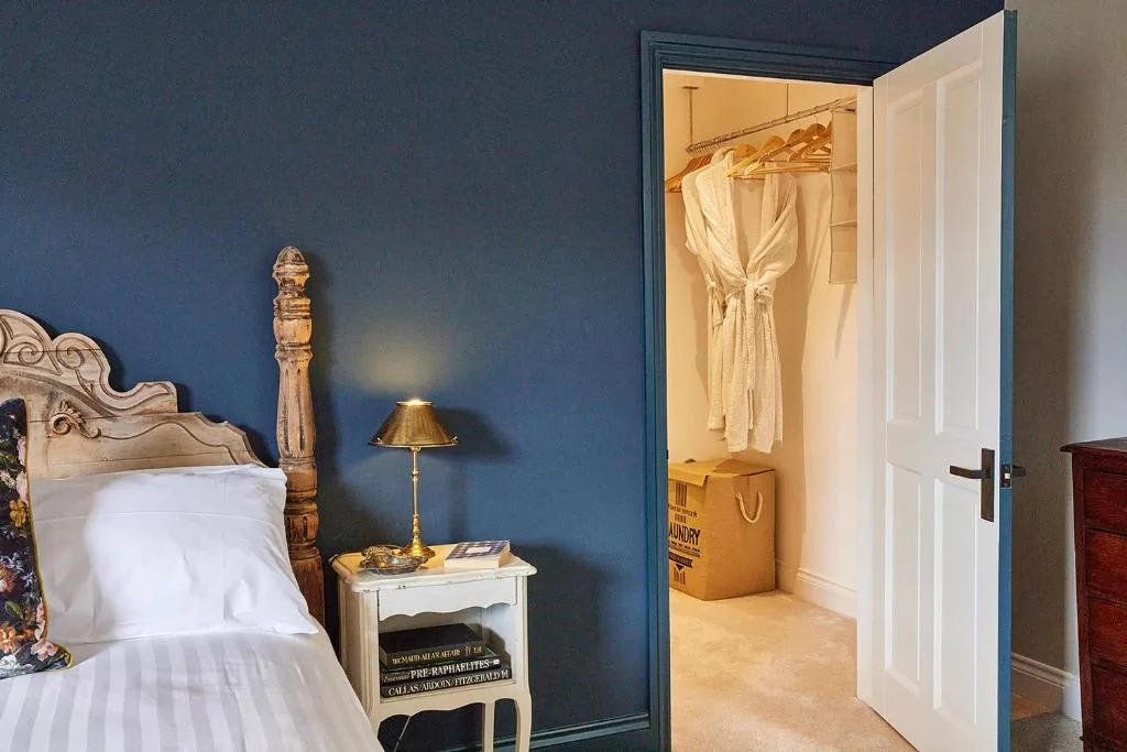 A bedroom with a bed beside an open closet containing hanging clothes.