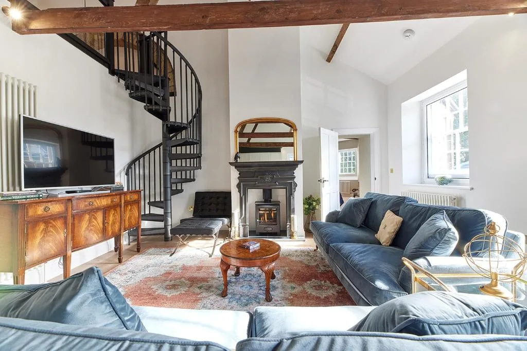 A bright living room with blue seating, a fireplace, and a spiral staircase.