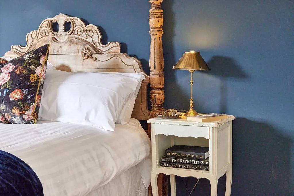 A bedroom with a white bed beside a small bedside table and lamp.