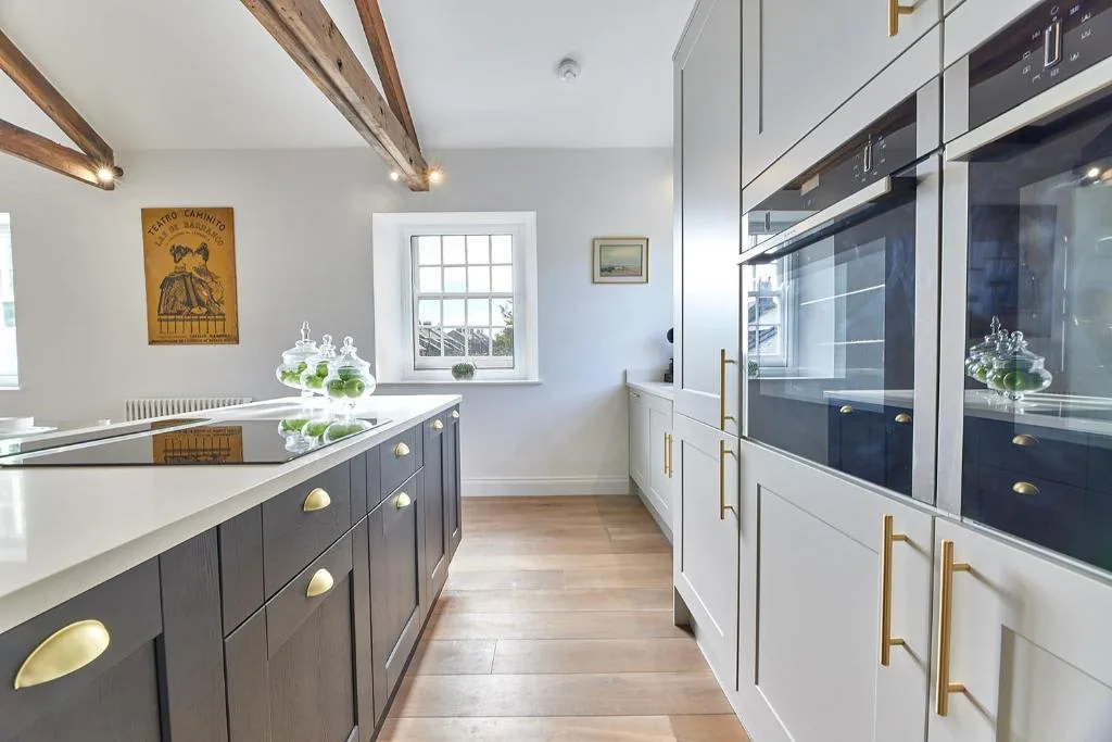 A bright modern kitchen with dark cabinetry, white counters, and built-in appliances.