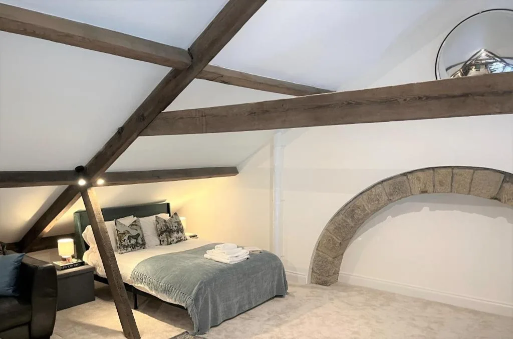 A bedroom with a bed beneath exposed wooden beams and a stone arch.