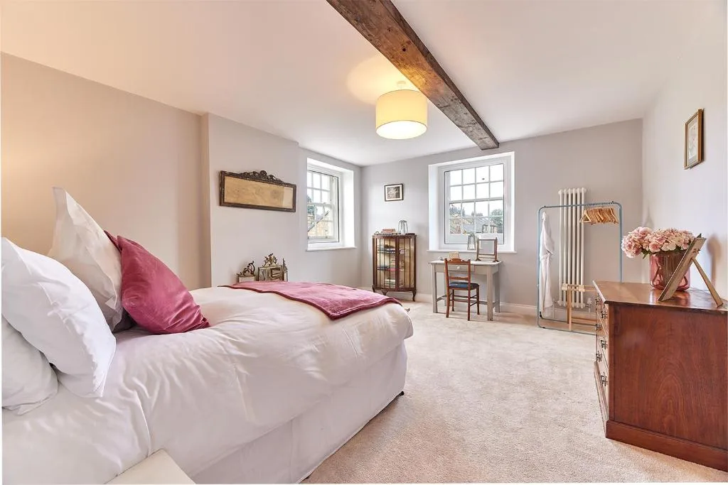 A bright bedroom with a bed, two windows, and a wooden dresser.