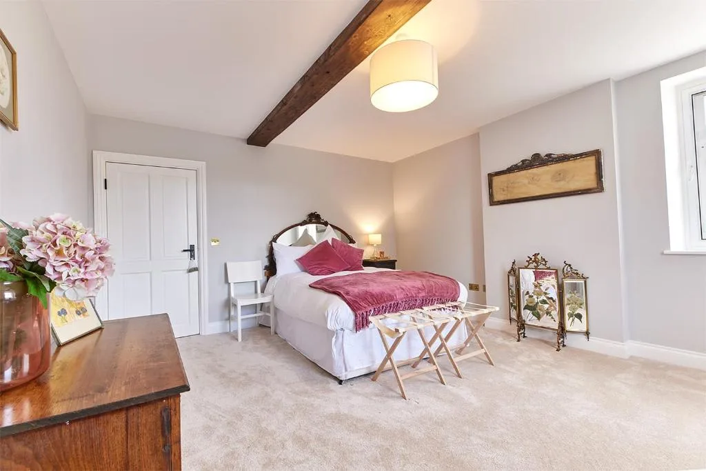 A bedroom with a bed dressed in white and burgundy linens.
