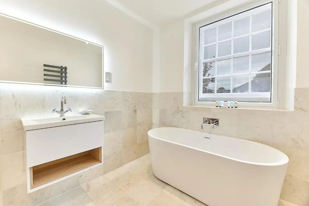 A bright bathroom with a freestanding bathtub, vanity, and large window.