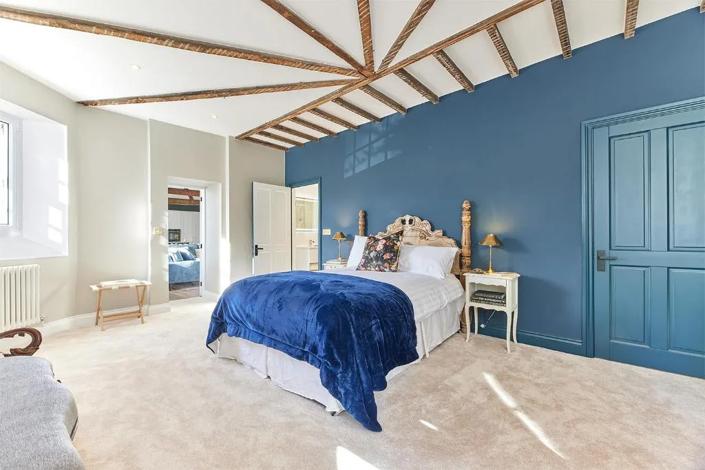 A bright bedroom with a bed dressed in blue against a blue wall.