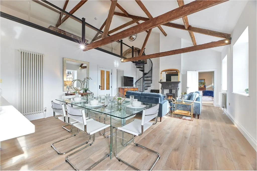 An open-plan living and dining room with a glass dining table and exposed wooden beams.