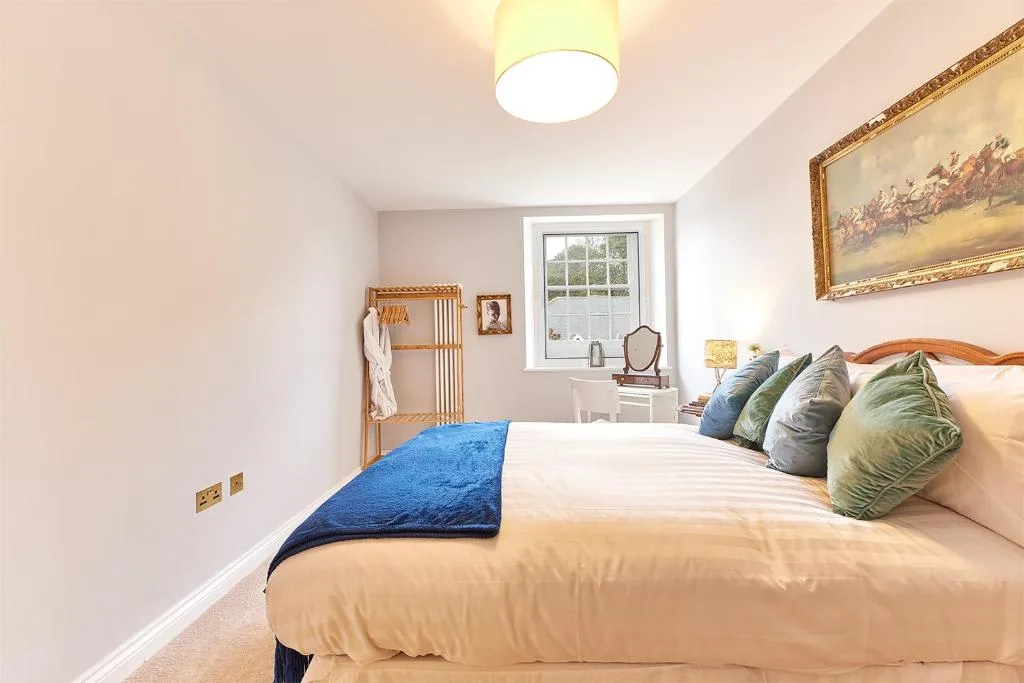 A bright bedroom with a neatly made bed and a window overlooking greenery.
