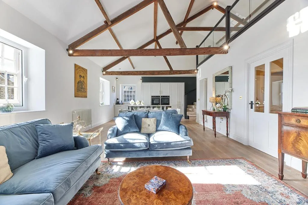 A bright living room with blue seating beneath exposed wooden ceiling beams.