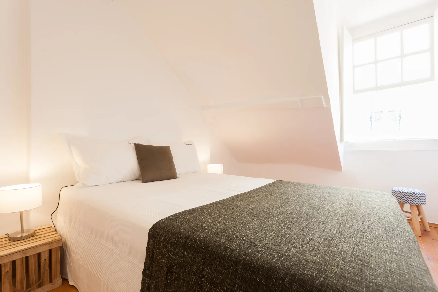 A bright bedroom with a bed beneath a sloped ceiling and a window.