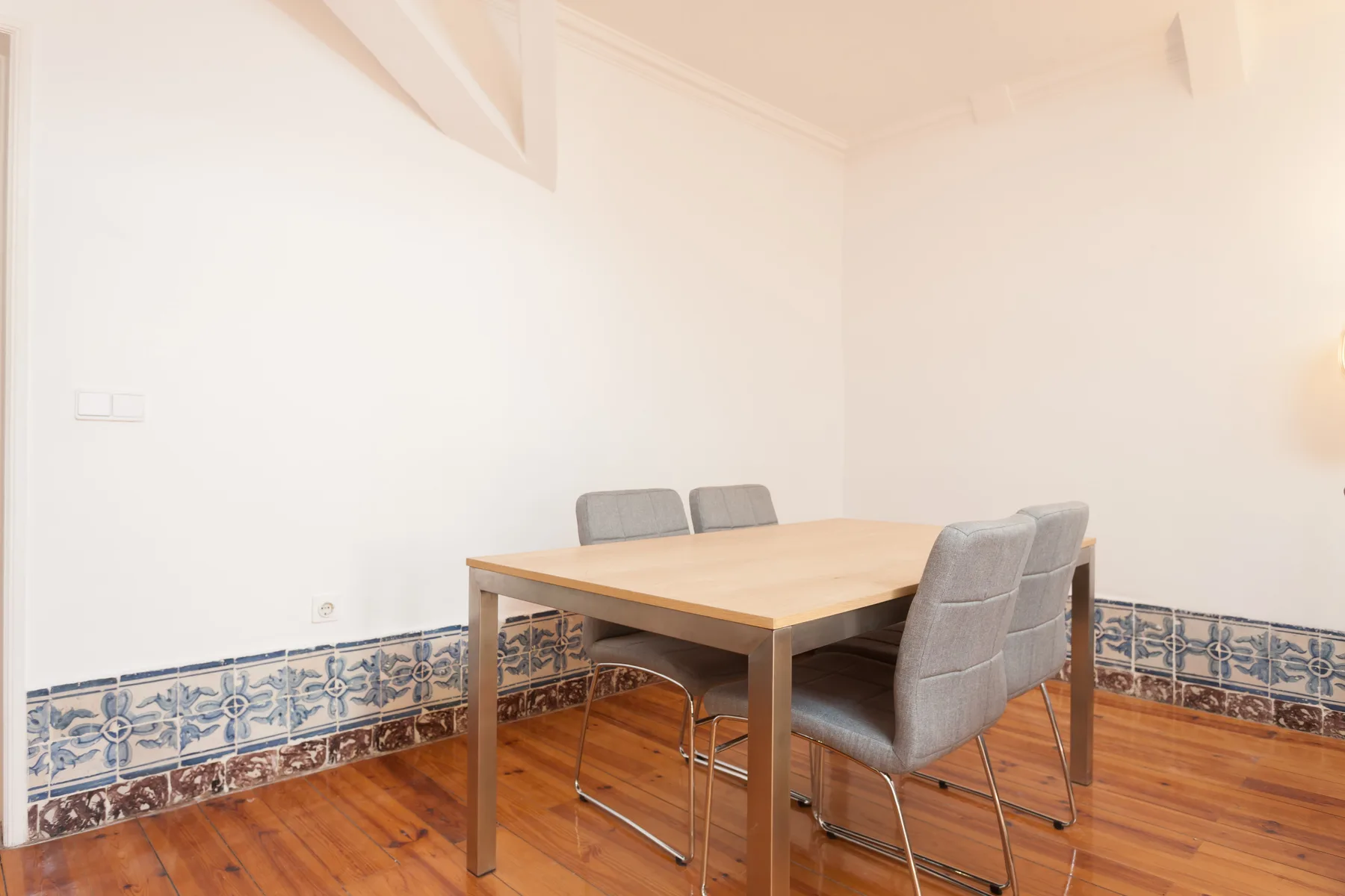 A dining area with a wooden table and gray seating against patterned tile.