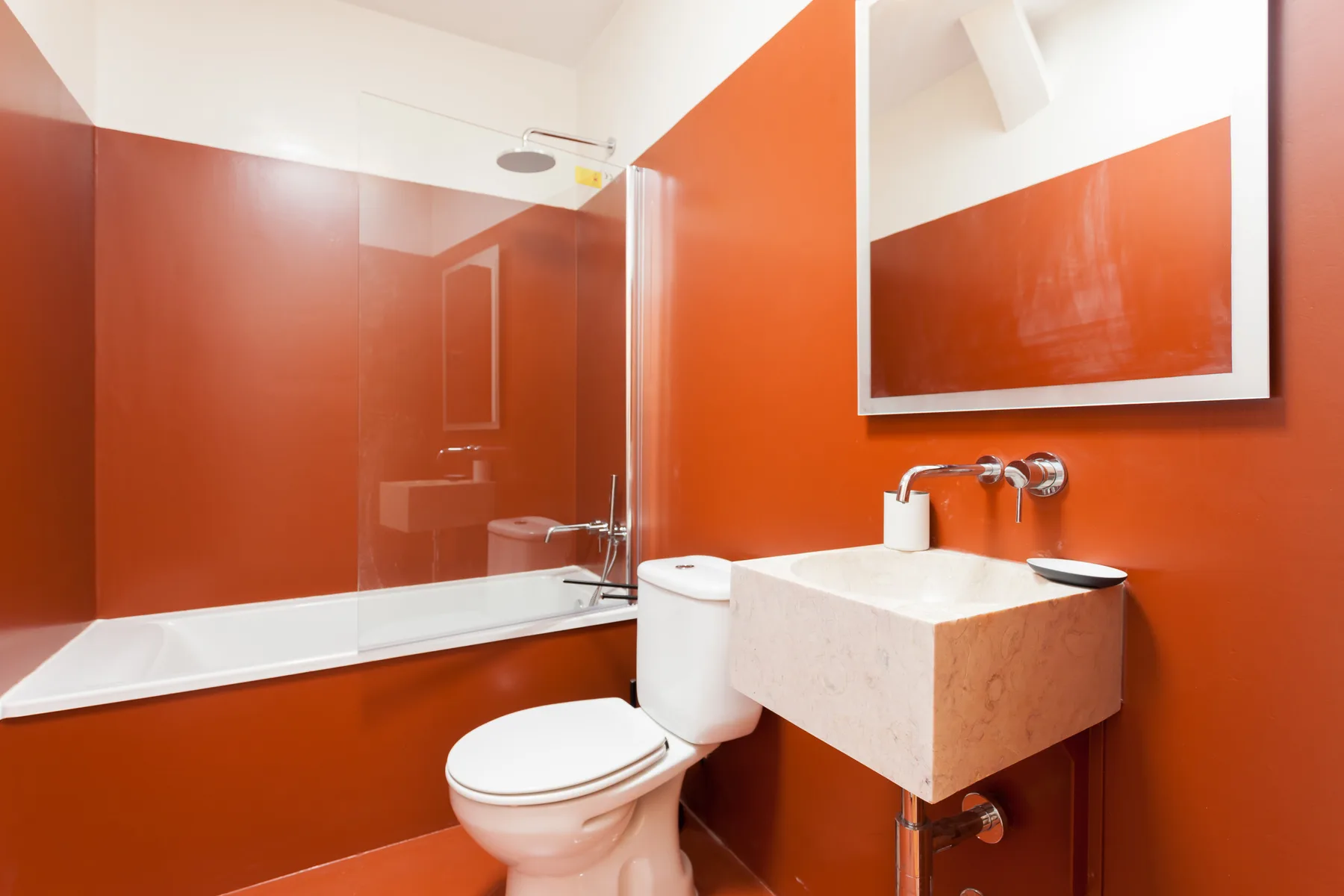A bathroom with a toilet, wall-mounted sink, and bathtub behind a glass panel.