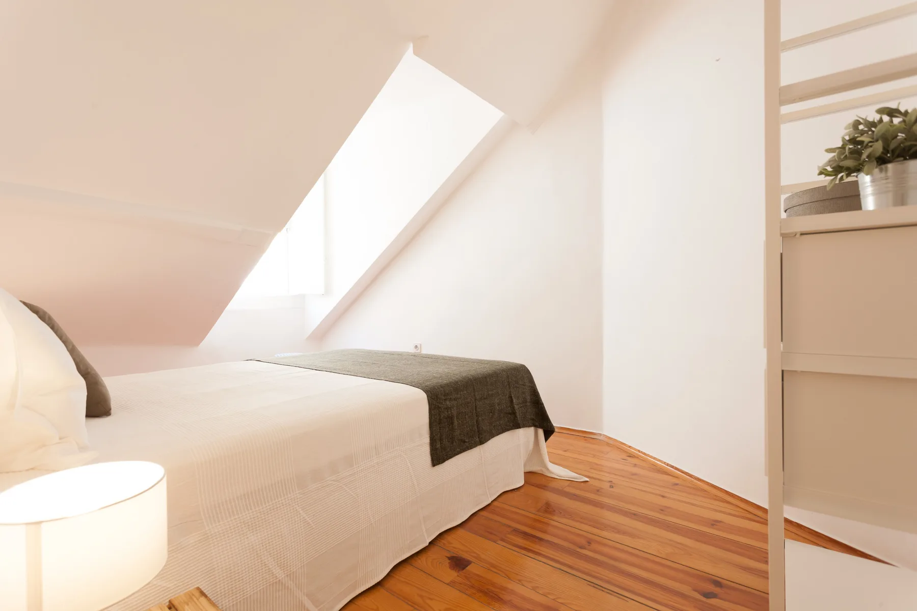 A bright bedroom with a bed beneath a sloped ceiling and a skylight.