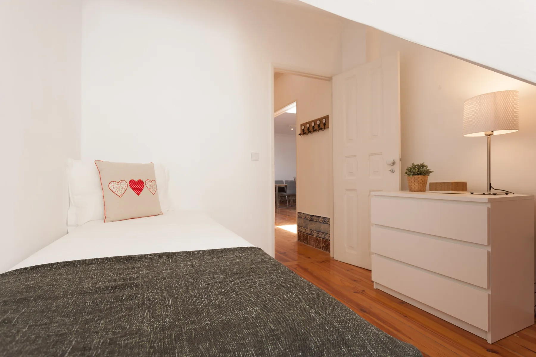A bedroom with a bed and a white dresser topped by a lamp.