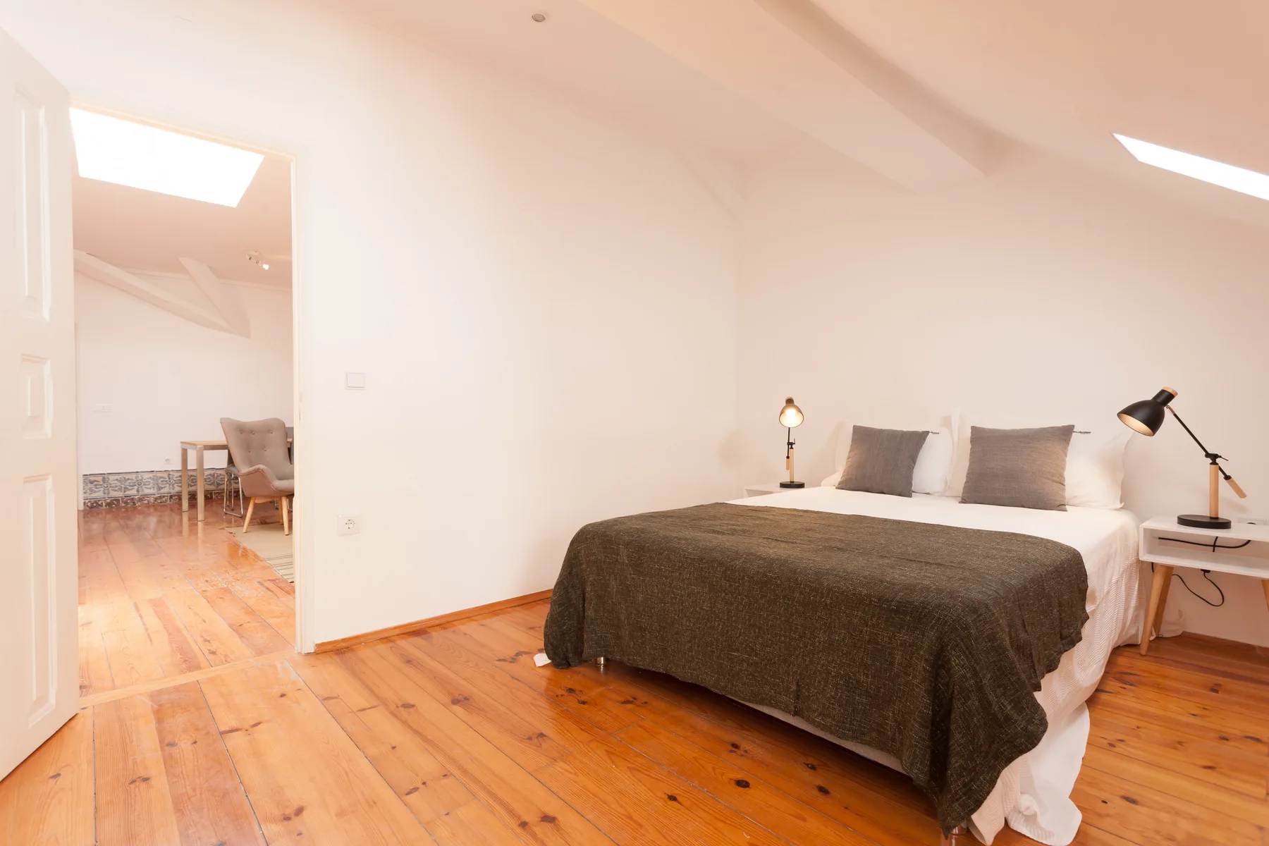 A bedroom with a bed and bedside lamps on a wooden floor.