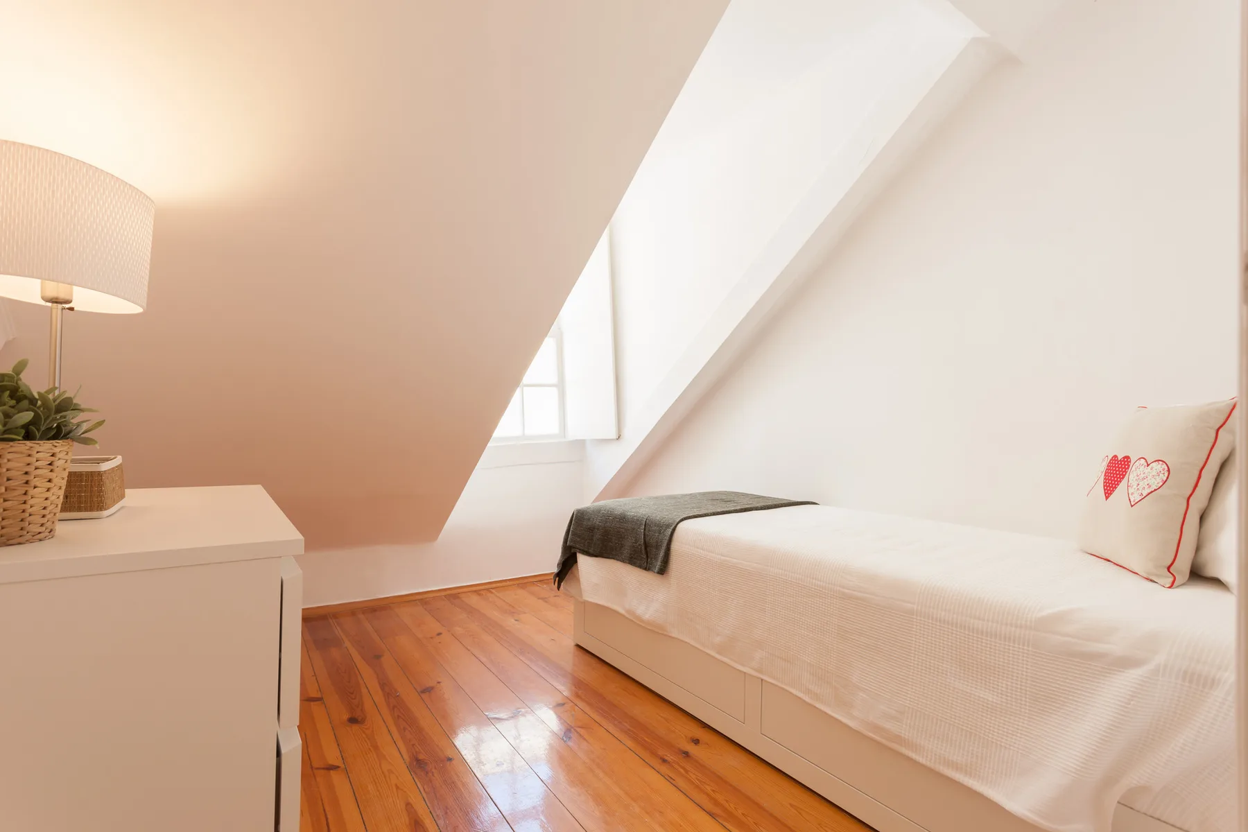 A bright bedroom with a single bed beneath a sloped ceiling.