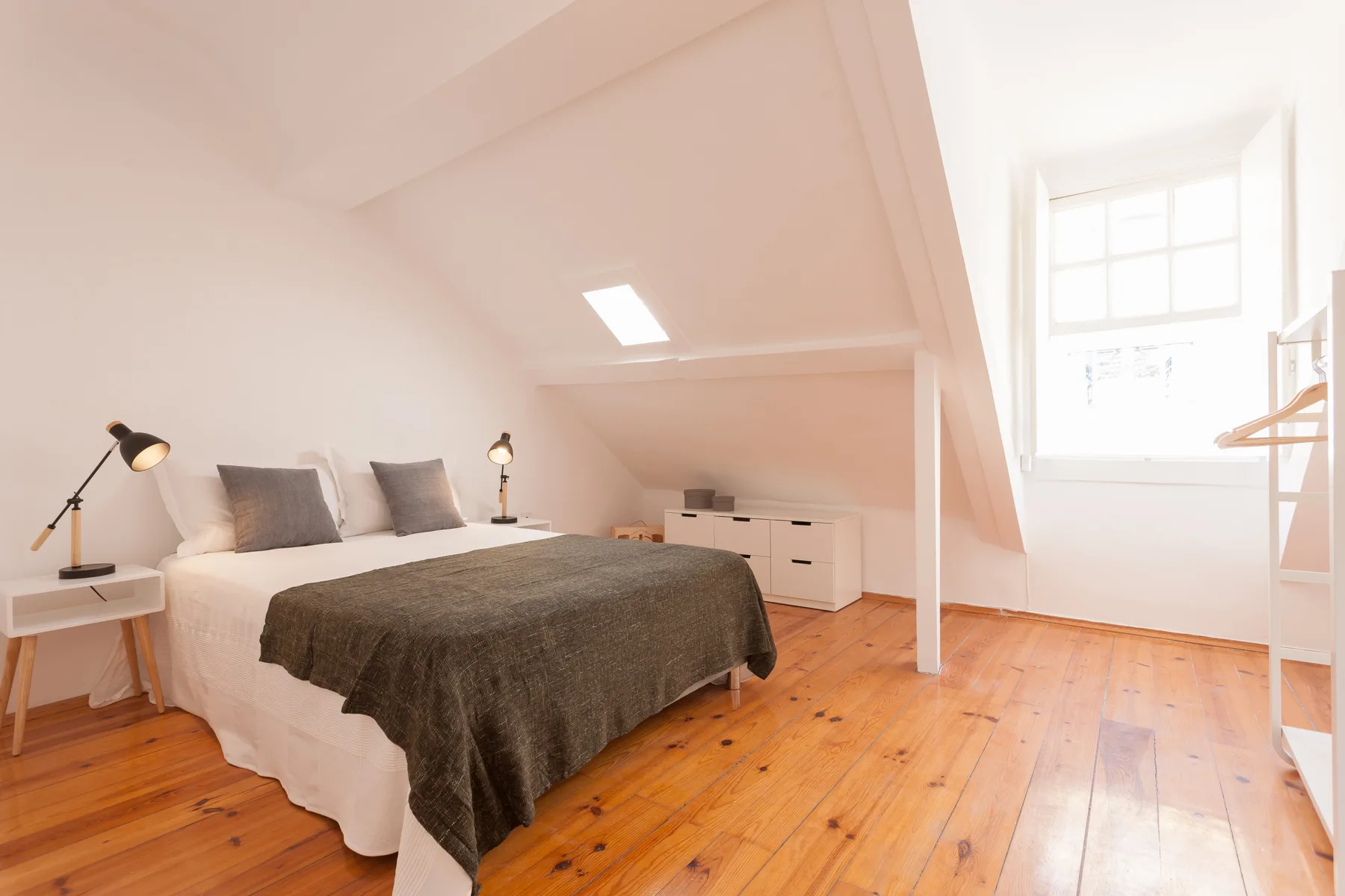 A bedroom with a bed, bedside lamps, and a bright window.
