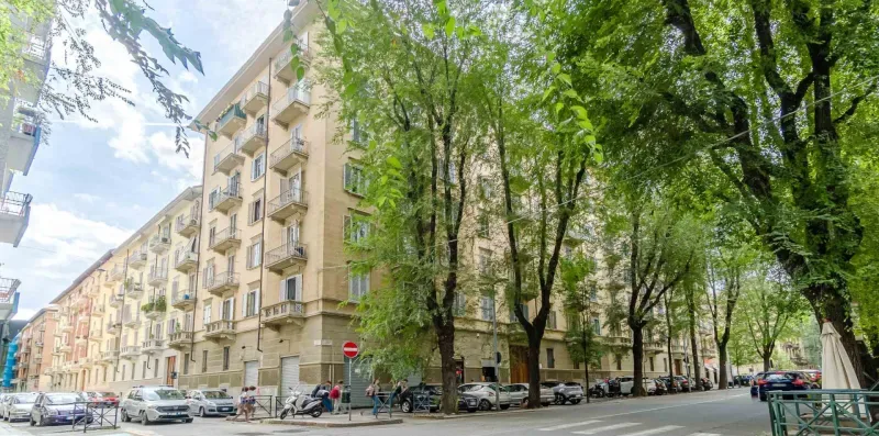 Una calle arbolada bordea una hilera de edificios de apartamentos y coches estacionados.