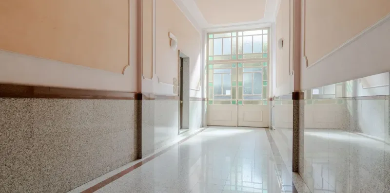Un pasillo luminoso con paredes inferiores de azulejos y una ventana grande al fondo.